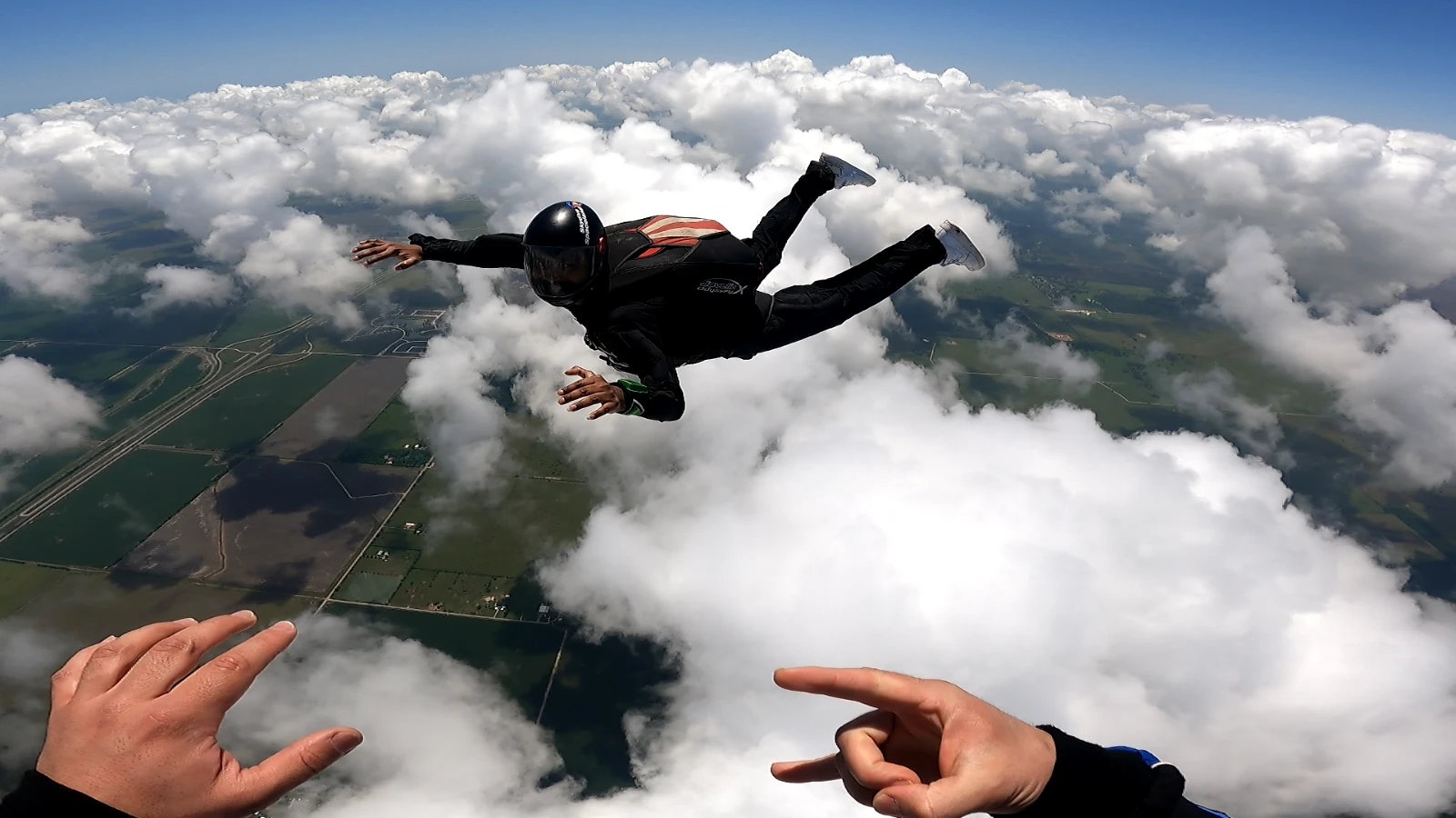 Bheeshma in freefall during AFF training, arms out over a deck of clouds, an instructor's hands signalling in the foreground